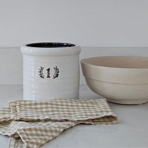 This handsome reproduction Old Stoneware Crock is inspired by early 20th century pottery found in farmhouses throughout the US. This reproduction crock has an white color with a black accents, making this piece a perfect accent for American farmhouse style kitchens. Use to store cooking utensils or display your favorite flowers. (Accents and Flowers not included) 6.6” Diam x 8”H