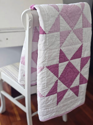 A modern take on the iconic sawtooth star quilt block, this organic cotton patchwork throw is hand quilted by skilled artisans. The antique-inspired design features pinkish-lilac and magenta stars with a playful pin dot pattern. Fully reversible, the quilt backing showcases a coordinating floral print. The Sweet Sawtooth Star Quilted Throw is finished with a playful scalloped binding. Use it to cozy up on the sofa or style it folded at the foot of a twin, full, or queen bed.