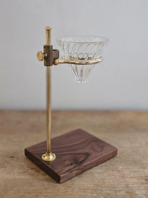 Crafted in the USA from brass in a lab-style, the Clerk Pour Over Coffee Stand brings a vintage touch to your kitchen. The clerk utilizes the Hario v60 glass pour-over (included) resting on the ring to adjust to the height of your mug or decanter. The ring adjusts using the brass slider on the rod (11 inches tall) to the height you need. The base is made of beautiful American walnut finished with a simple food-safe coating.
