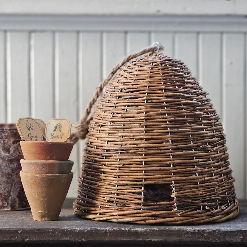 Bee Skeps are perfect for obtaining the look of an old English Country Garden. This Willow Bee Skep makes a great addition to any tabletop or bookcase, as the handwoven quality lends a beautiful texture to any decor. Let this natural Bee Skep make a charming addition to your farmhouse décor. Features a fully enclosed skep with a little door and a jute rope for hanging if desired. 10" Diam x 10"H