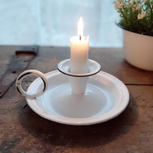 Add that centuries old farmhouse look to any bedside bureau or tabletop with our White Chamberstick Taper Candle Holder. It has the classic finger loop and tray, which made it easy to carry candles from room to room back in the day. The white enamel finish adds a sweet cottage feel. Taper candle not included.  5"W x 2½"H