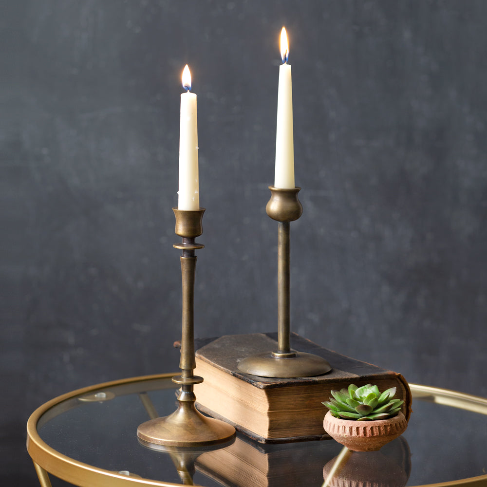 This Aged Brass Finish Taper Candle Holder Set brings timeless style to any tabletop. The old brass style finish has a time-worn patina, inspired by antique shop finds. This set of two features different style necks, both with a slender, elegant design. Add to a bookshelf, bedside table, or create a stunning centerpiece on a long farm table by weaving a few among a garland of greenery. Candles not included.