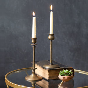 This Aged Brass Finish Taper Candle Holder Set brings timeless style to any tabletop. The old brass style finish has a time-worn patina, inspired by antique shop finds. This set of two features different style necks, both with a slender, elegant design. Add to a bookshelf, bedside table, or create a stunning centerpiece on a long farm table by weaving a few among a garland of greenery. Candles not included.