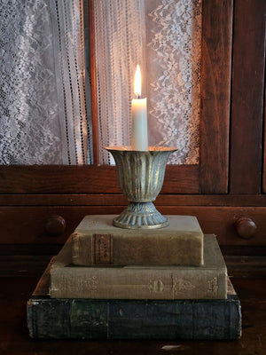 Our Aged Gold Fluted Urn Taper Candle Cup features a distressed gold metal finish with an ornate scalloped design. The cup sits on a pedestal and has plenty of space between the holder and the sides, making it the perfect choice for displaying a candle ring! The candle cup has vintage style and is ideal for catching dripping wax. Measures 3.75" in diameter and 4"H and holds a standard taper (candle not included).