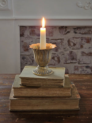 Our Aged Gold Fluted Urn Taper Candle Cup features a distressed gold metal finish with an ornate scalloped design. The cup sits on a pedestal and has plenty of space between the holder and the sides, making it the perfect choice for displaying a candle ring! The candle cup has vintage style and is ideal for catching dripping wax. Measures 3.75" in diameter and 4"H and holds a standard taper (candle not included).