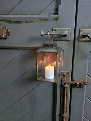 The Aged Iron Lantern adds rustic ambiance to any occasion.&nbsp; Features an antique bronze style finish and glass windows to protect the flame. Includes a door on one side and a wire handle for hanging. Makes a beautiful tabletop presentation. Holds one pillar candle. Each sold separately.