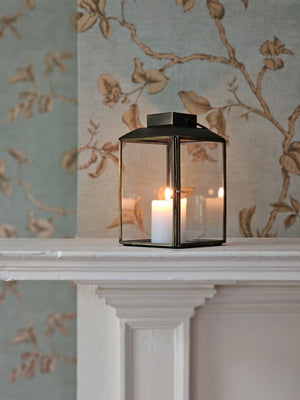 The Aged Iron Lantern adds rustic ambiance to any occasion.&nbsp; Features an antique bronze style finish and glass windows to protect the flame. Includes a door on one side and a wire handle for hanging. Makes a beautiful tabletop presentation. Holds one pillar candle. Each sold separately.