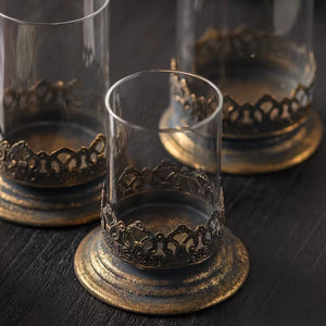 The Antiqued Gold and Glass Candle Hurricanes are an elegant set of three candle holders that features beautifully detailed metal bases with an antique black and gold finish. Perfect for adding warm ambiance and a touch of vintage charm to living rooms, dining tables, or event decor.