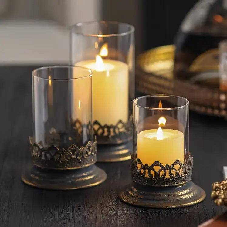 The Antiqued Gold and Glass Candle Hurricanes are an elegant set of three candle holders that features beautifully detailed metal bases with an antique black and gold finish. Perfect for adding warm ambiance and a touch of vintage charm to living rooms, dining tables, or event decor.