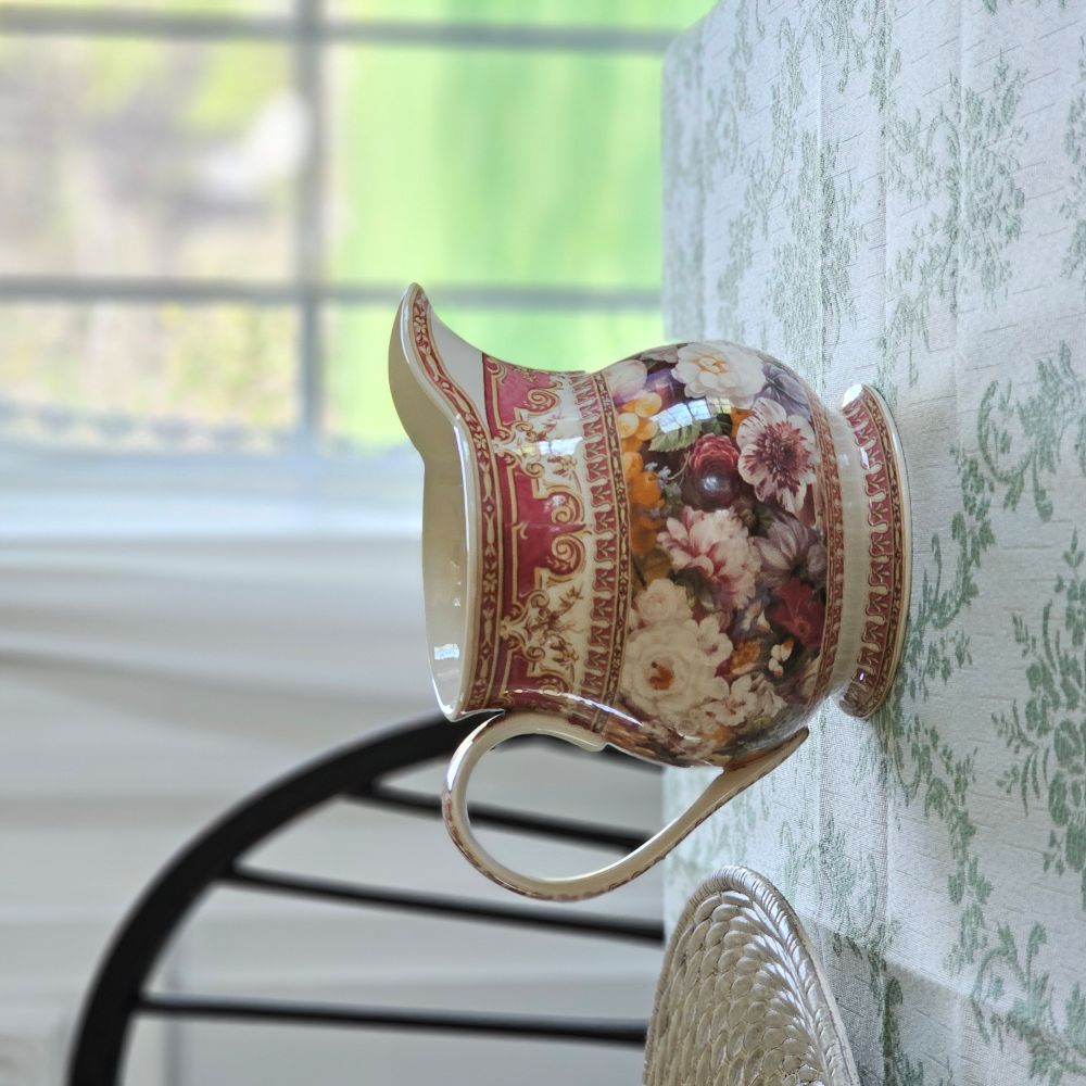 The Antique Style Old World Floral Pitcher brings a touch of elegance and vintage romance to any occasion. This porcelain pitcher features a richly detailed floral design, highlighted by a warm, cream-toned glaze that gives the piece a soft, antique-inspired appearance. The base color is not a bright white, but rather a subtle ivory/cream tone that enhances the depth and character of the intricate floral artwork and ornate border detailing.