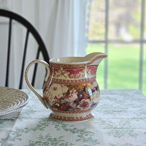 The Antique Style Old World Floral Pitcher brings a touch of elegance and vintage romance to any occasion. This porcelain pitcher features a richly detailed floral design, highlighted by a warm, cream-toned glaze that gives the piece a soft, antique-inspired appearance. The base color is not a bright white, but rather a subtle ivory/cream tone that enhances the depth and character of the intricate floral artwork and ornate border detailing.