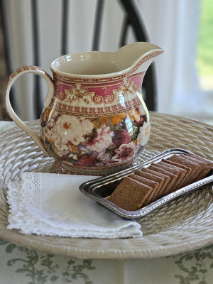 The Antique Style Old World Floral Pitcher brings a touch of elegance and vintage romance to any occasion. This porcelain pitcher features a richly detailed floral design, highlighted by a warm, cream-toned glaze that gives the piece a soft, antique-inspired appearance. The base color is not a bright white, but rather a subtle ivory/cream tone that enhances the depth and character of the intricate floral artwork and ornate border detailing.