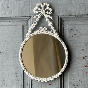 The Antoinette Bow Mirror is brimming with ornate details that add instant ambiance to any room. The distressed white mirror brings charming reflections with its lovely metal frame featuring an attractive bow and ribbon design. 7.75" x 12.75"H