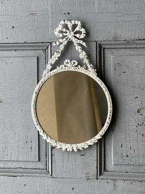 The Antoinette Bow Mirror is brimming with ornate details that add instant ambiance to any room. The distressed white mirror brings charming reflections with its lovely metal frame featuring an attractive bow and ribbon design. 7.75" x 12.75"H