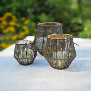 This set of three black wire lanterns, with a gold coating on the inside, adds an eye-catching, sophisticated look to tabletops. When lit, the candle light is amplified by the gold to create an enchanting glow, while the wire cage creates a magical dance with the light. These lanterns will bring a warm, cozy touch to any home. Set of three. Holds 3" diam pillar candle.