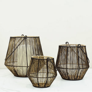 This set of three black wire lanterns, with a gold coating on the inside, adds an eye-catching, sophisticated look to tabletops. When lit, the candle light is amplified by the gold to create an enchanting glow, while the wire cage creates a magical dance with the light. These lanterns will bring a warm, cozy touch to any home. Set of three. Holds 3" diam pillar candle.