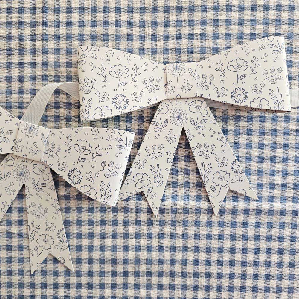 Add sweet cottage charm to any occasion with our Paper Bow Garland with Blue Floral Design.&nbsp;Made of high-quality paper, the garland features eight white bows with a delicate floral design hung along a cream grosgrain ribbon. Perfect for country weddings, baby showers, or garden parties. Spring into style with this beautiful banner!