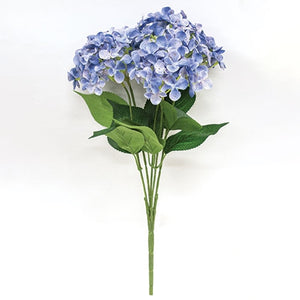 The Blue Hydrangea Bush Pick showcases exquisite blue fabric petals paired with fresh green leaves, creating a refined summer accent. Its flexible plastic stem supports bright hydrangea blooms subtly touched with soft white hues, adding depth and elegance. Measuring 17” long by 10” wide and 5” deep, this floral pick brings a sophisticated touch to any arrangement or decor.
