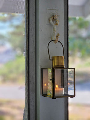 Bring the warmth of flickering candlelight to your home or garden with our Bristol Brass Tealight Lantern. The antique brass style finish offers a coastal cottage feel with old-world charm. The glass windows protect the flame. Includes a door on one side and a wire handle for hanging. Makes a beautiful tabletop presentation. Suitable for indoor or outdoor use. Holds one tealight candle. Each sold separately. Includes one lantern.