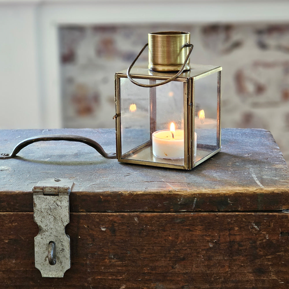 Bring the warmth of flickering candlelight to your home or garden with our Bristol Brass Tealight Lantern. The antique brass style finish offers a coastal cottage feel with old-world charm. The glass windows protect the flame. Includes a door on one side and a wire handle for hanging. Makes a beautiful tabletop presentation. Suitable for indoor or outdoor use. Holds one tealight candle. Each sold separately. Includes one lantern. 3"L x 3"W x 4.75"H