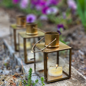 Bring the warmth of flickering candlelight to your home or garden with our Bristol Brass Tealight Lantern. The antique brass style finish offers a coastal cottage feel with old-world charm. The glass windows protect the flame. Includes a door on one side and a wire handle for hanging. Makes a beautiful tabletop presentation. Suitable for indoor or outdoor use. Holds one tealight candle. Each sold separately. Includes one lantern. 3"L x 3"W x 4.75"H