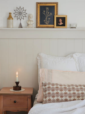 Bedroom with wooden nightstand, decorative pillows, and framed artwork on the shelf.