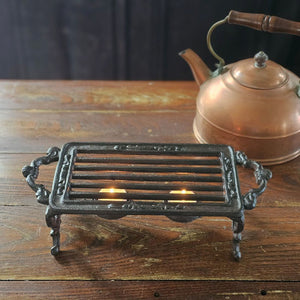 The Cast Iron Pot Warmer Trivet is perfect for adding an old-time touch with tons of practicality. This rectangular cast iron trivet is designed to keep teapots and food dishes warm. It features two tea light candle holders under the grill and an antique brown finish.