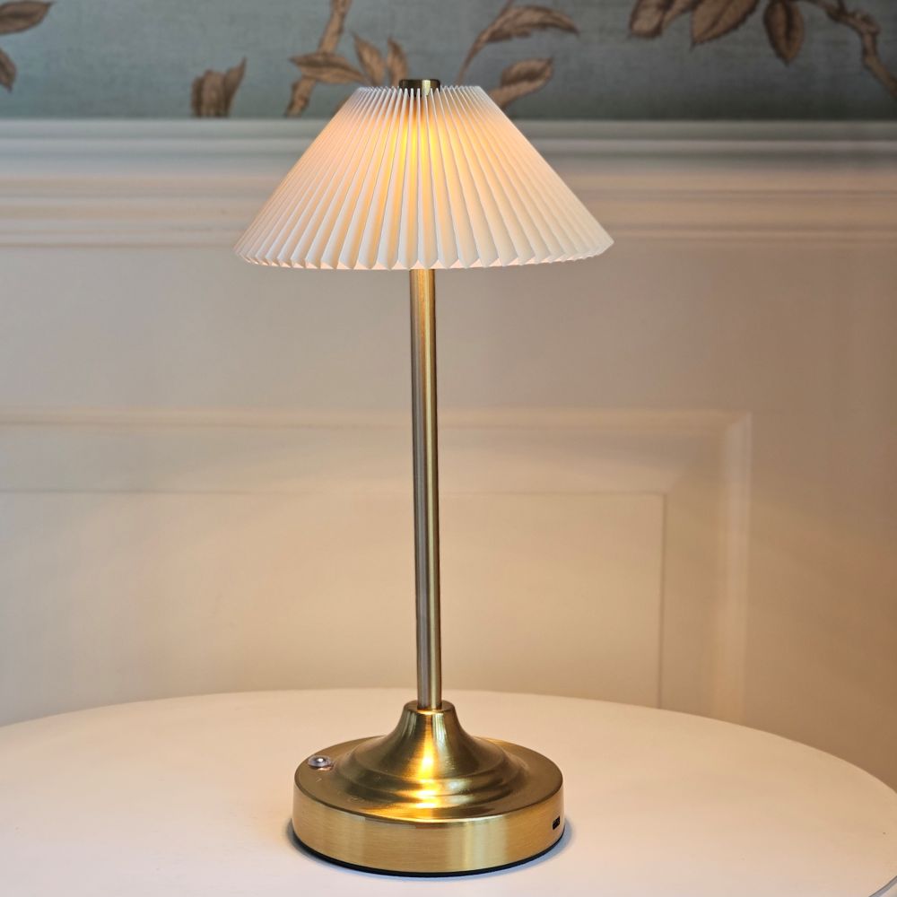 This elegant Cordless Gold Lamp is ideal for bedside tables and countertops, offering a warm LED glow beneath a cream pleated shade. Its built-in rechargeable battery ensures portability. Requires USB charging cable (not included). 6.3 X 6.3 X 12.8