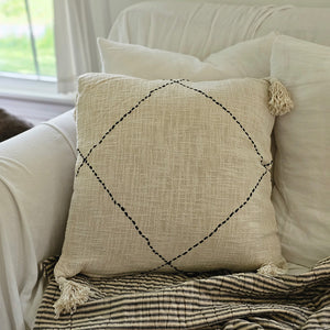 Whether it's on a bed or a cozy chair, you won't be able to resist this pillow's amazing texture. The Creamy Beige Accent Pillow with Black Stitching offers relaxed farmhouse elegance with its rustic look and fringed tassels.  The super soft fabric has an earthy, chunky weave, accented by a chunky black stitched design. Features a zippered closure for easy removal and care. Hand wash. 100% Cotton. Includes insert. 20" x 20"