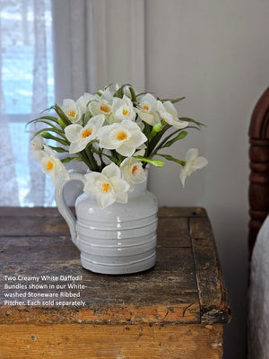 White ceramic pitcher with artificial white daffodils on a wooden surface