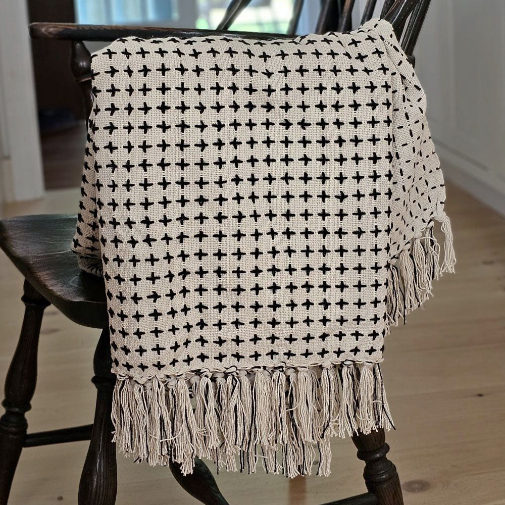 The Cross Stitched Reversible Throw Blanket is perfect for cuddling up on the couch or your favorite book nook. Designed to feel just as warm as your softest knitted sweater, it's made with 100% premium cotton – known for its lasting quality and soft textured feel.&nbsp; It features a unique reversible design with a cream cotton knit and black stitched cross geometric pattern that gives this throw handsome character with a vintage camp feel. The fringed edges add relaxed elegance. 