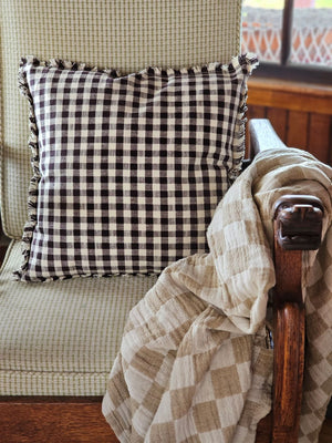 Enhance your living space with the Dark Brown Gingham Pillow, where timeless country charm meets refined design. Crafted from 100% cotton with a subtle off-white and dark brown gingham pattern, this pillow features elegant fringe edging and a discreet, easy-to-remove zipper. Its plush polyester insert offers both comfort and structure, making it a sophisticated accent that brings warmth and texture to any room. Spot clean only to preserve its quality. Measuring 18" x 18"