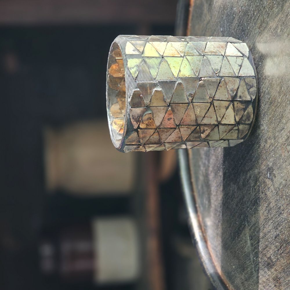 Add a bit of magical ambiance with our Mercury Glass Mosaic Candle Holder. Features aged mirrored glass that sparkles with silver, rose and golden hues. The mirrored glass also picks up the hues of the room decor, making this piece blend in effortlessly with its surroundings. The shimmering glow of candlelight through the cut pattern is dreamy. Holds one votive candle. 2.75" Diam x 3.25"H