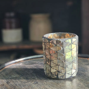 Add a bit of magical ambiance with our Mercury Glass Mosaic Candle Holder. Features aged mirrored glass that sparkles with silver, rose and golden hues. The mirrored glass also picks up the hues of the room decor, making this piece blend in effortlessly with its surroundings. The shimmering glow of candlelight through the cut pattern is dreamy. Holds one votive candle. 2.75" Diam x 3.25"H