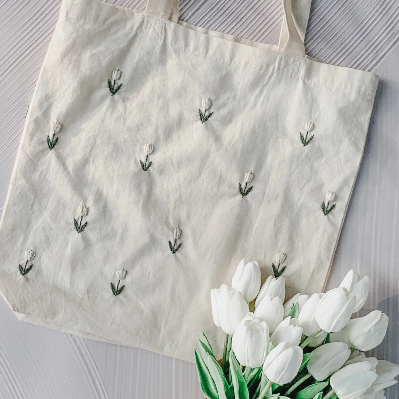 The Embroidered Tulip Tote Bag is perfect for groceries, shopping excursions or a day at the beach. Handmade White Embroidered tulips with dark green stems make this tote bag a charming option for daily use.100% cotton. Machine wash. Embroidered in the USA. 14.5 x 14.5in Tote bag with 10.5 in handles