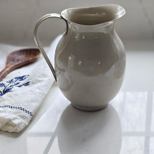 Bring the easy charm of country cottage living to your farmhouse with our Enamel Pitcher in Mushroom. The simple allure of enamelware fits right in with any decor, but every farmhouse needs at least one piece. Inspired by flea market finds, our vintage style enamel pitcher features a warm tan/grey finish for an old stone look . Food safe. Pitcher measures 5" diam x 7.5"H 