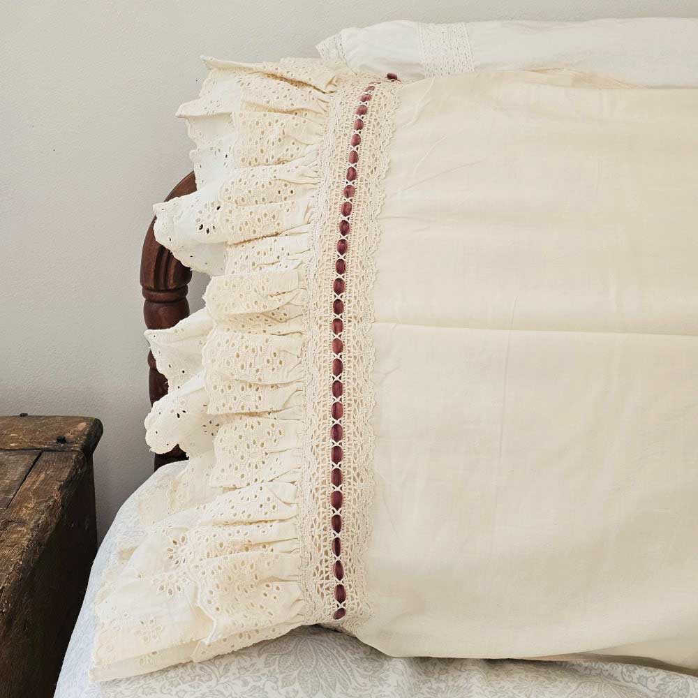 Our Eyelet Ruffles with Velvet Ribbon Pillowcase, Set of Two lends dreamy cottage style to any bedroom. These cream pillowcases feature a double layer of ruffle edges with exquisite floral eyelet detail with a dark rose velvet ribbon woven through a crochet border. The cream color is warm, falling on the yellow spectrum. This lace edge pillowcase will add texture and a charming vintage look to your room.