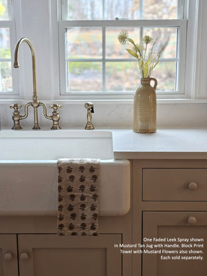 Kitchen with white sink, gold faucet, and vase with flowers on countertop.