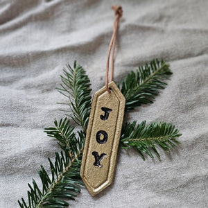 Enhance your holiday decor with our Gold Joy Tag Ornament Set. Each ornament features a durable leather loop for easy hanging and can be used to add a special touch to your gifts or adorn your tree. Celebrate the season with this elegant and versatile tag. Set of three.