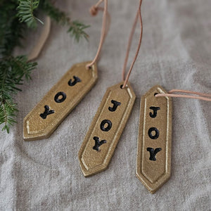 Enhance your holiday decor with our Gold Joy Tag Ornament Set. Each ornament features a durable leather loop for easy hanging and can be used to add a special touch to your gifts or adorn your tree. Celebrate the season with this elegant and versatile tag. Set of three.