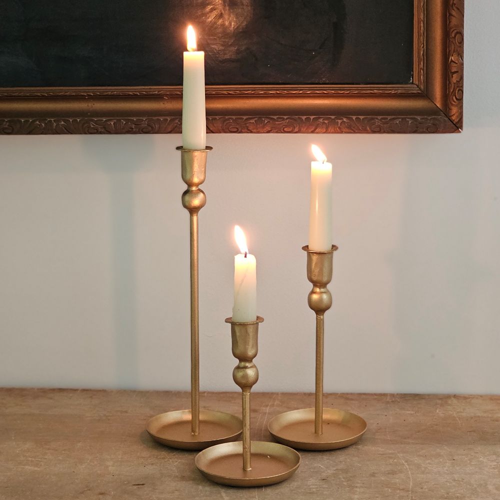 Our Golden Taper Candle Holder Set lends simple elegance to any occasion. This set of three taper candle holders feature a slender, classic design with a bottom tray for catching wax. The bright gold metallic finish brings fresh, vibrant style. Add to a bookshelf, bedside table, or create a stunning centerpiece on a long farm table by weaving a few among a garland of greenery. Holds regular tapers.