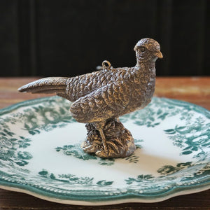 The Golden Pheasant Ornament features an artfully distressed gold finish and intricate feather detailing that evokes vintage charm and sophistication. Add timeless elegance to your tree or use as a gift topper. Made of resin and generously sized, it makes stunning nature-inspired display.