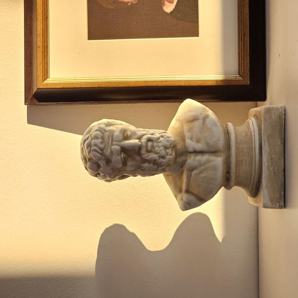 Small plaster bust of a bearded figure on a wall with a framed picture above