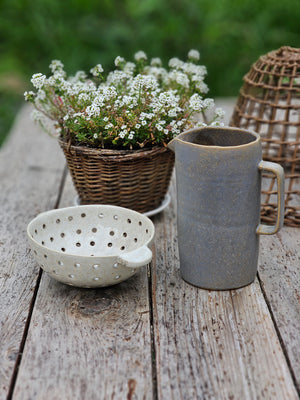 Our Grey Glaze Ceramic Pitcher captures the essence of a quiet foggy morning. A layered glaze of umber and blue gives this ceramic pitcher a cozy mottled texture and misty grey hue. It adds a minimalist touch to your farmhouse with a relaxed beauty that comes from its perfectly imperfect hand-shaped look. Shown with our Ceramic Colander Bowl