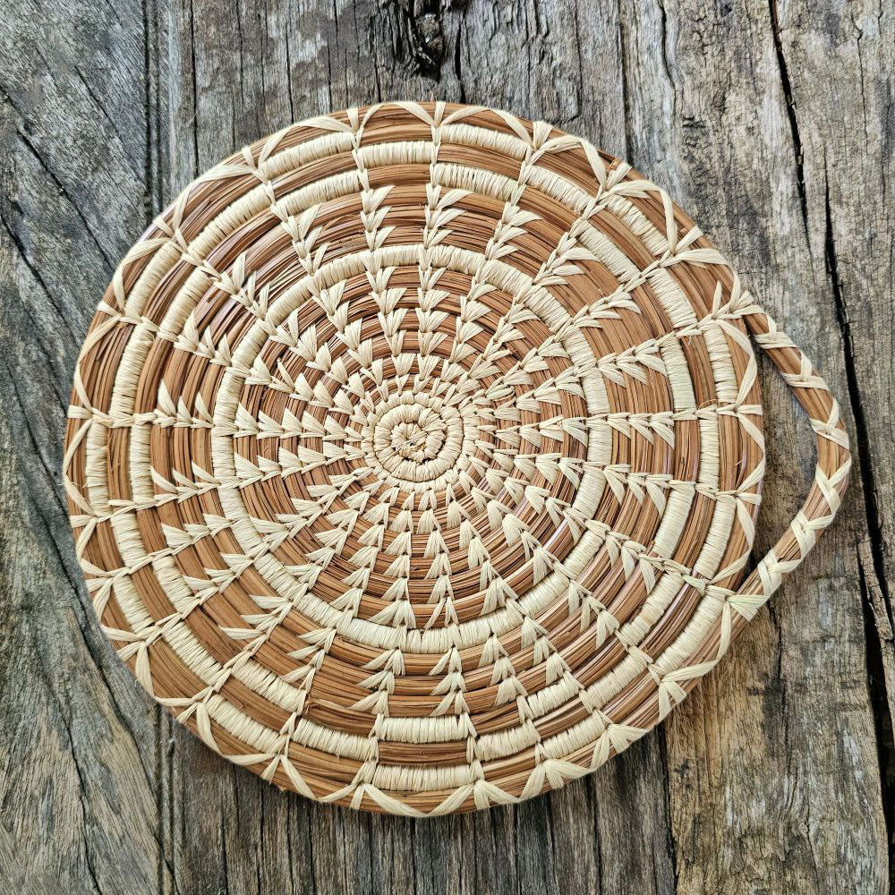 The Handwoven Cloud Forest Trivet is intricately stitched by basket makers from long-leaf pine needles, this heat resistant trivet is perfect to set on your table to protect it from hot dishes, and lovely displayed on the wall when not being used. Created of sustainable pine needles by women using time-honored techniques, these fair trade pieces support economic development and education for the makers through a dedicated nonprofit partnership. Woven raffia and pine needle designs may vary.