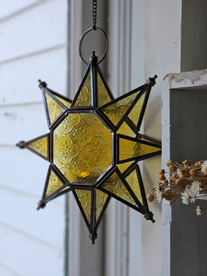 Let it glow! This charming Hanging Embossed Glass Star Candle Holder brings old-world ambiance to any room. This glass star light features embossed detail panes of yellow glass between an antiqued copper style metal framework. It holds one tealight candle (not included) and hangs from a chain. 