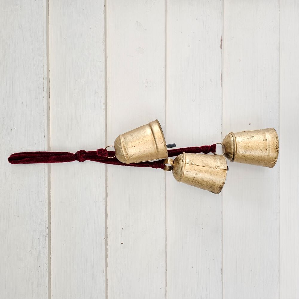 Add warmth and sparkle to your home decor with our Hanging Gold Bell Cluster with Velvet Ribbon. Each metal bell features a rustic feel with aged golden finish. The lush velvet ribbon hanging a dark maroon red. Add to wreaths and greenery or keep it simple by displaying them just as they are. Includes three bells.