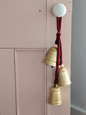 Add warmth and sparkle to your home decor with our Hanging Gold Bell Cluster with Velvet Ribbon. Each metal bell features a rustic feel with aged golden finish. The lush velvet ribbon hanging a dark maroon red. Add to wreaths and greenery or keep it simple by displaying them just as they are. Includes three bells.