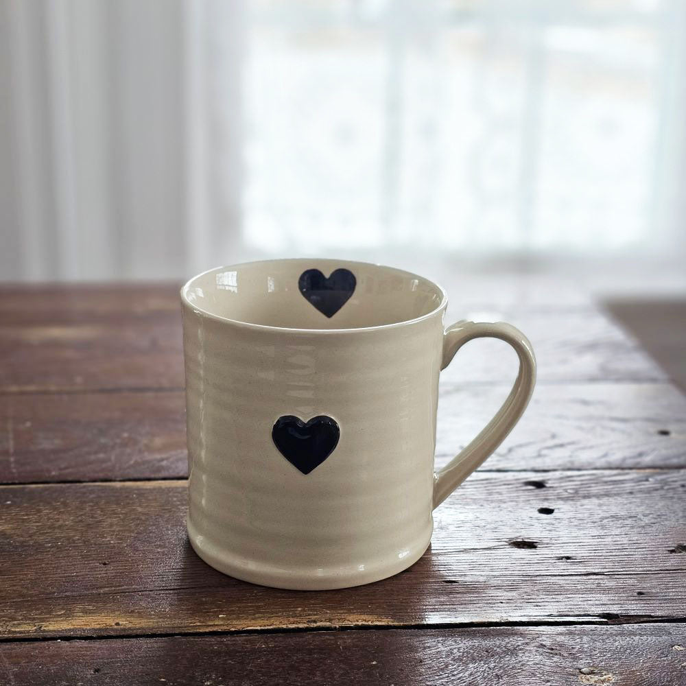 Every sip from our Rustic Heart Mug is a reminder to slow down and appreciate the simple things in life. This stoneware mug is the perfect shape to hold, and the hand-painted hearts spread a little love. Features a rustic light beige glaze with a raised black heart on the outer portion of the mug and a painted black heart on the inside as well.