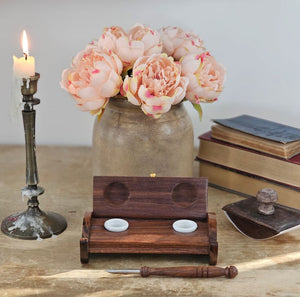 The Inkwell Stand with Porcelain Inkwells and Wood Nib Pen Set makes a perfect desk accessory reminiscent of early Colonial days. The set features a wood inkwell stand that opens and closes, two white porcelain inkwells, a wood nib writing pen, and a bag black ink powder so you can easily get started.